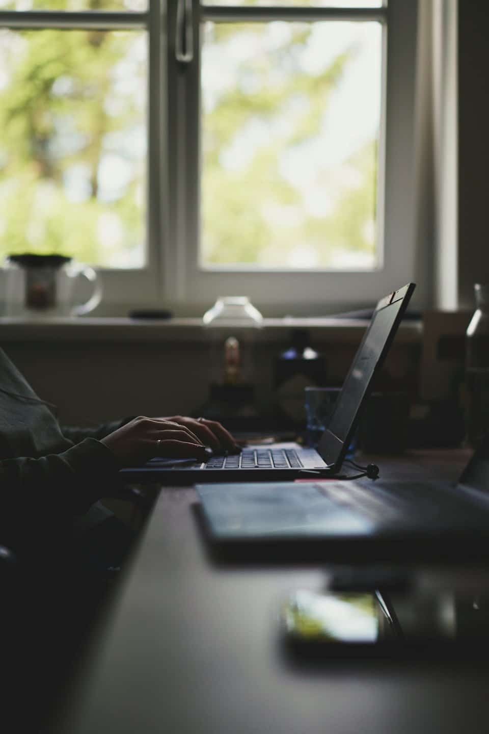 Una persona digita su un computer portatile a una scrivania di legno.