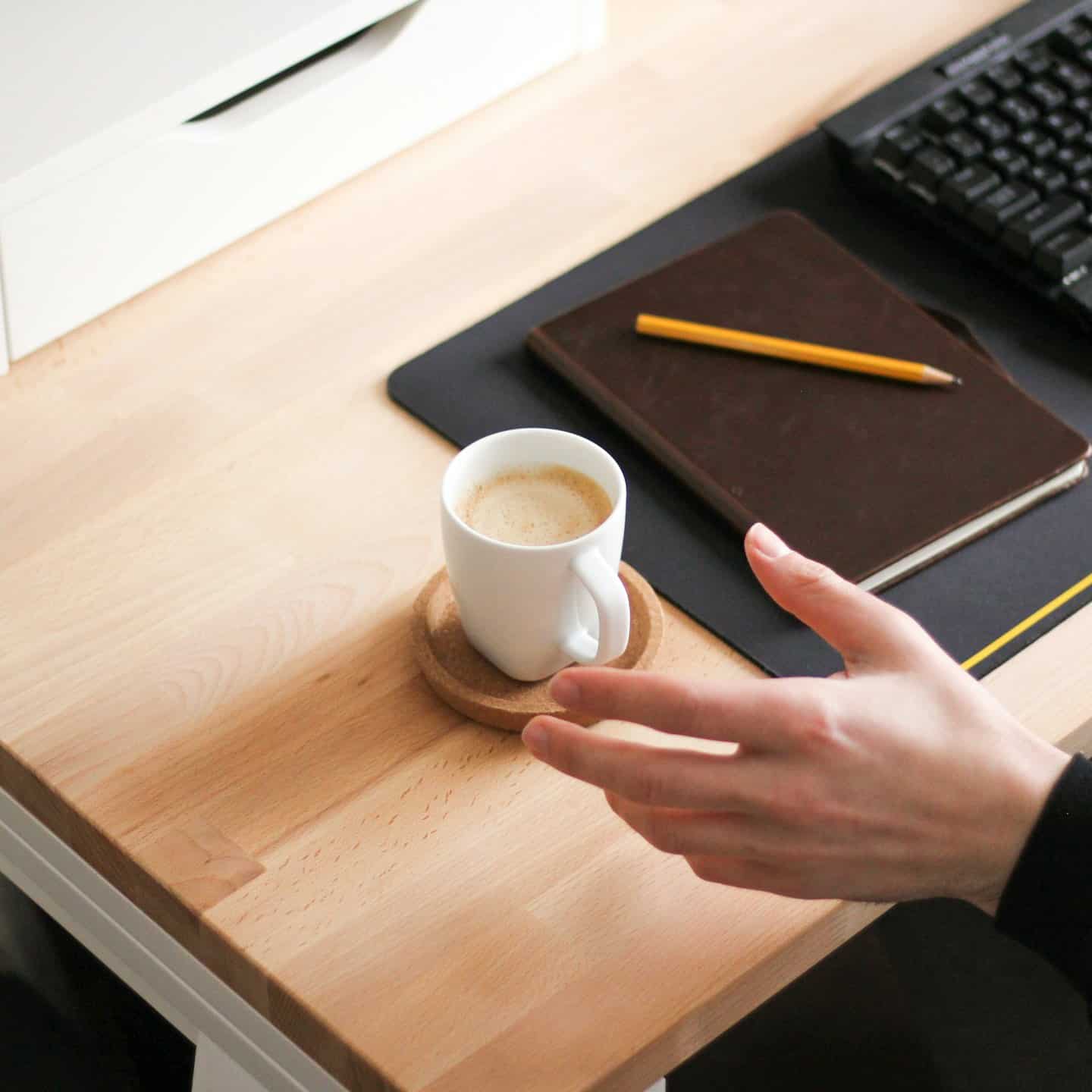 Mano che afferra una tazza di caffè su una scrivania di legno ordinata.